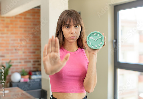 young pretty woman looking serious showing open palm making stop gesture. alarm clock concept