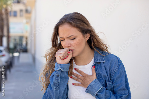 pretty hispanic woman feeling ill with a sore throat and flu symptoms, coughing with mouth covered