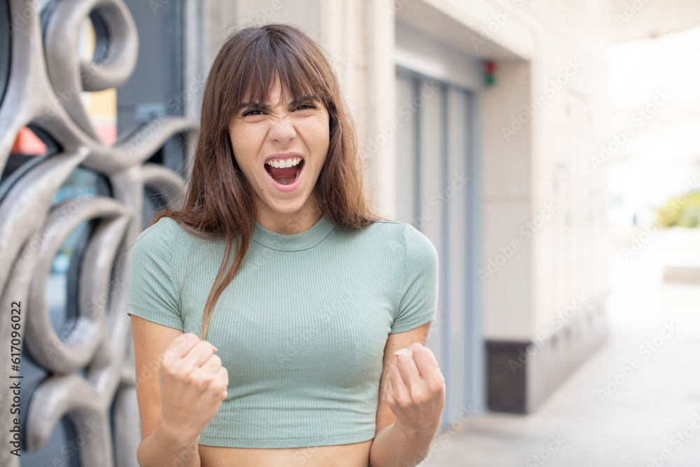 pretty young woman shouting aggressively with annoyed, frustrated, angry look and tight fists, feeling furious