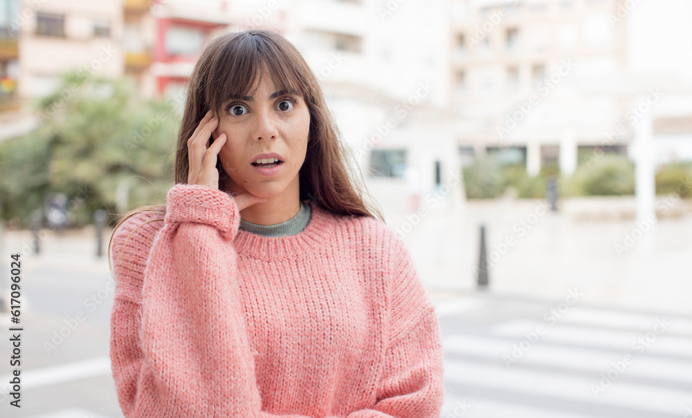 pretty young woman open-mouthed in shock and disbelief, with hand on cheek and arm crossed, feeling stupefied and amazed pretty young woman open-mouthed in shock and disbelief, with hand on cheek and arm crossed, feeling stupefied and amazed
