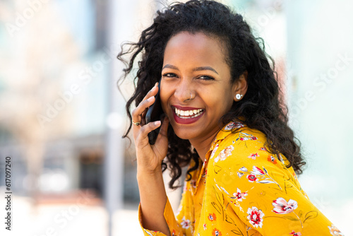 Beautiful young african woman talking on mobile phone and smiling outside