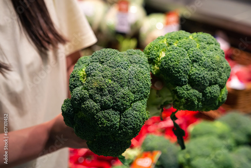 The woman holds broccoli in the store or in the market, close up.