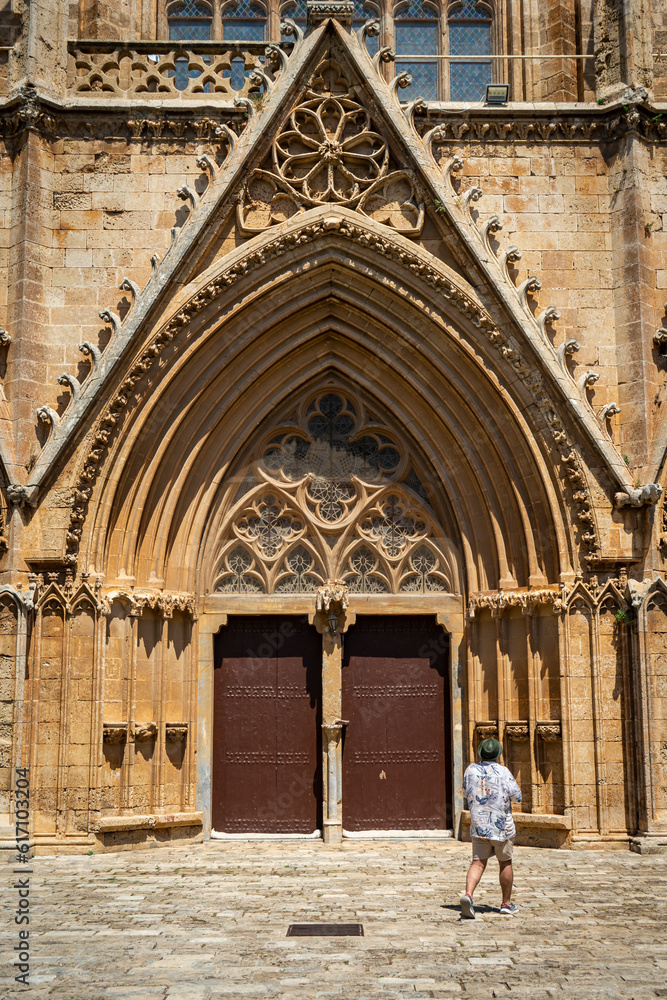 Lala Mustafa Pasha Camii Mosque or old Cathedral of Saint Nicholas in Famagusta or Gazimagusa historical city centre with a tourist in front, Northern Cyprus. Selective focus. Lala Mustafa Pasha Camii Mosque or old Cathedral of Saint Nicholas in Famagusta or Gazimagusa historical city centre with a tourist in front, Northern Cyprus. Selective focus.