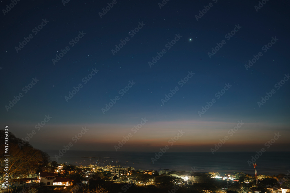 Illuminated coastal town by seascape under starry sky during nighttime at Costa Rica Illuminated coastal town by seascape under starry sky during nighttime at Costa Rica