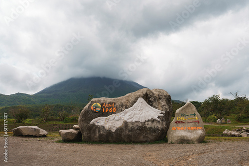 Rocks with sign of arenal 1968 trail and directional arrows in front of mountain volcano covered in clouds at Costa Rica photo