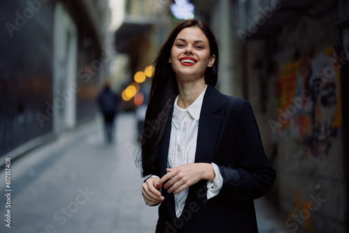 Fashion woman smile with teeth portrait tourist in stylish clothes in jacket with red lips walking down narrow city street flying hair, travel, French style, cinematic color, retro vintage style.