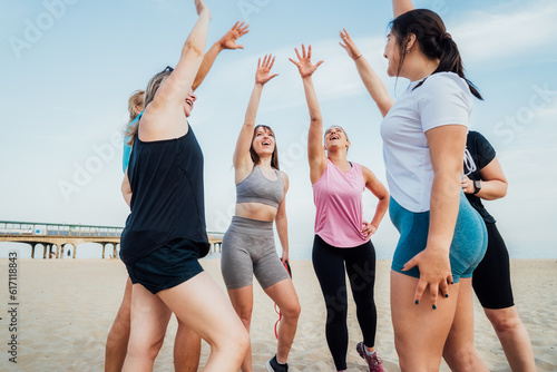 Happy fitness class giving high five after completing workout on beach. Multi aged women motivated after session together, engaged in team building, join hands for shared goal or success at training