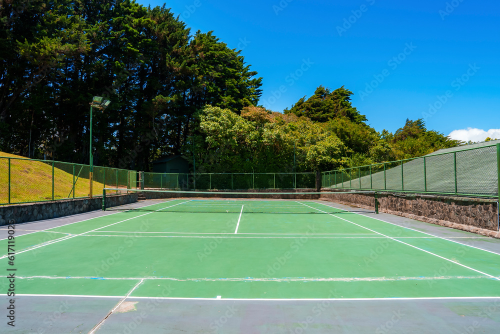Empty outdoor tennis court with net and boundary fence surrounded with lush green trees at Costa Rica