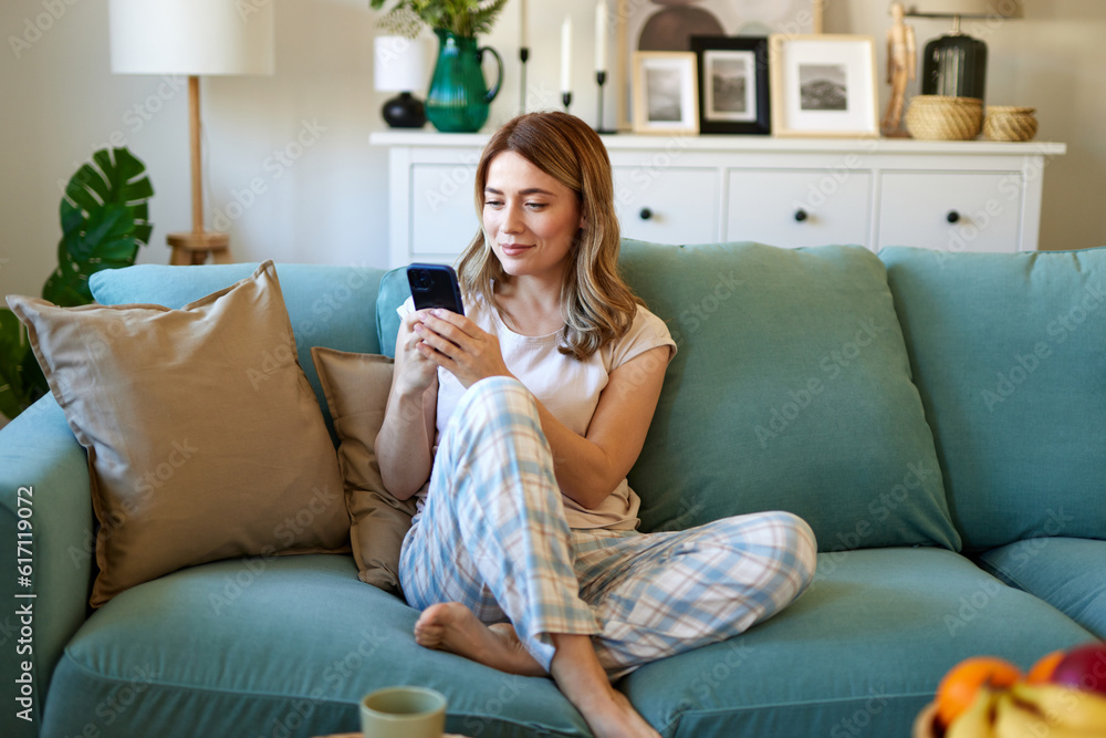 Happy woman text messaging on mobile phone while relaxing in the living room at home Happy woman text messaging on mobile phone while relaxing in the living room at home