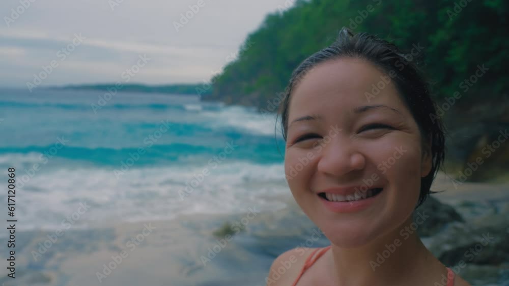Happy Japanese girl with sand in her hair after swimming in looks at the sea and turn her head smiles and camera and smiles from happiness. Woman against background of wild beach. Slow motion. 4k Happy Japanese girl with sand in her hair after swimming in looks at the sea and turn her head smiles and camera and smiles from happiness. Woman against background of wild beach. Slow motion. 4k