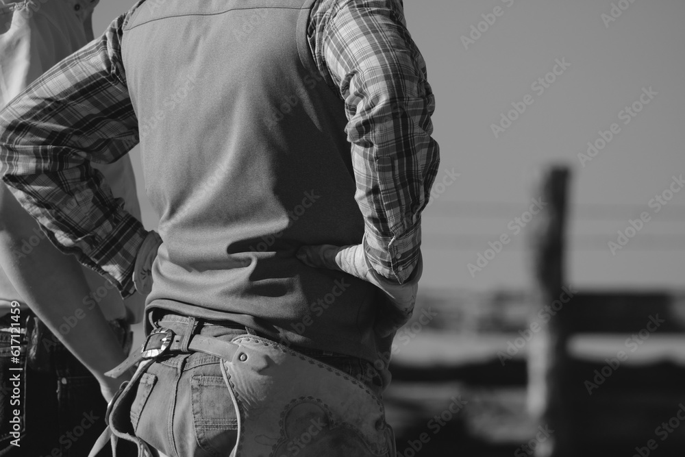 Fototapeta premium Western lifestyle shows cowboy on ranch in black and white, hands on hips.