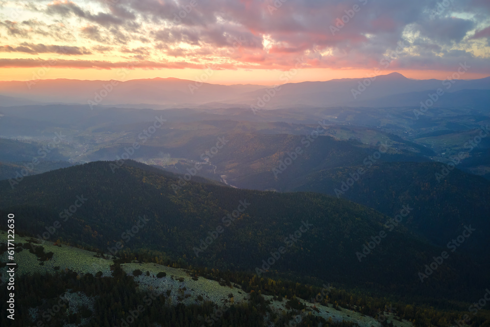 Aerial view of amazing scenery with foggy dark mountain peak covered with forest pine trees at autumn sunrise. Beautiful wild woodland with shining rays of light at dawn Aerial view of amazing scenery with foggy dark mountain peak covered with forest pine trees at autumn sunrise. Beautiful wild woodland with shining rays of light at dawn