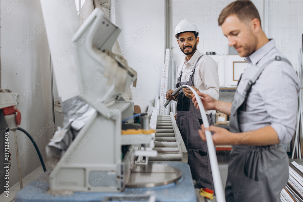 An international team, two workers work at a machine at a factory of PVC windows and doors An international team, two workers work at a machine at a factory of PVC windows and doors