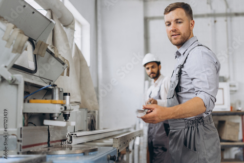 An international team, two workers work at a machine at a factory of PVC windows and doors