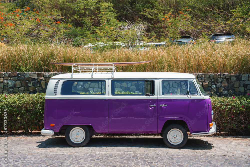 Classic purple colored parked van with surfboard on roof rack on a bright sunny day at Costa Rica. Travel and vacation concept