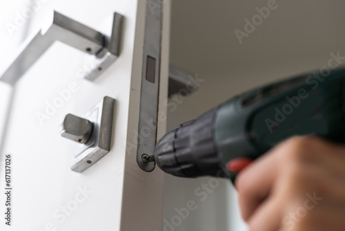 A locksmith is repairing an interior door lock. Close-up of male hands repairing or replacing an entrance door lock with a hex screwdriver