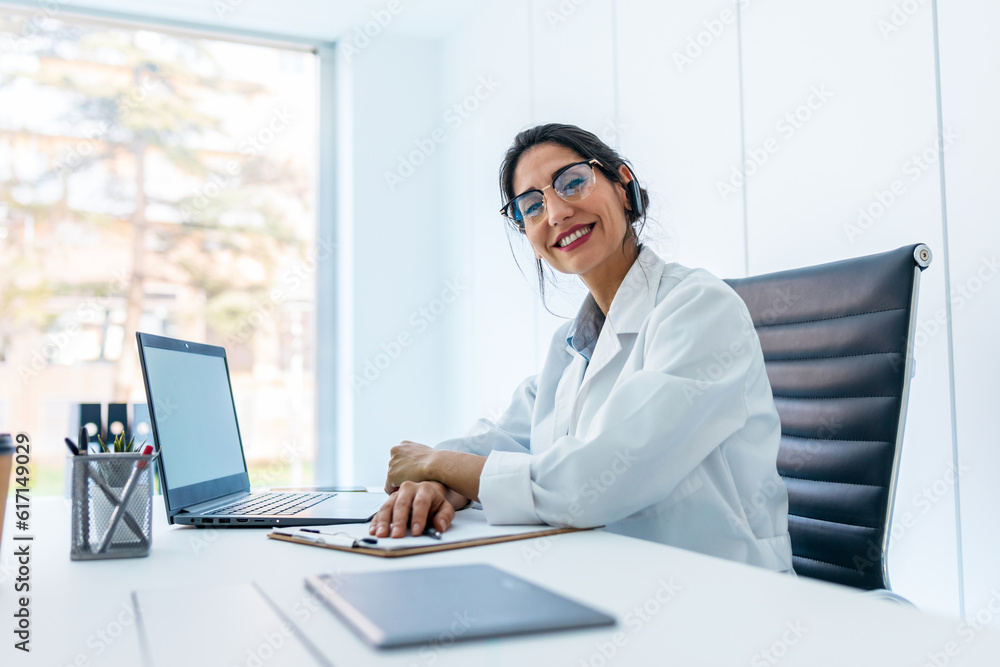 Beautiful female doctor doing a video call while talking with earphone in the medical consultation. Beautiful female doctor doing a video call while talking with earphone in the medical consultation.