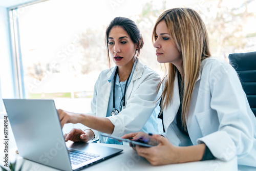 Two beautiful female doctors working with her laptop while talking in the medical consultation
