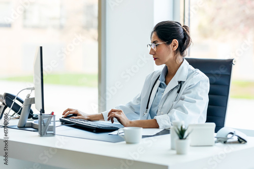 Beautiful female doctor working with computer in medical consultation.