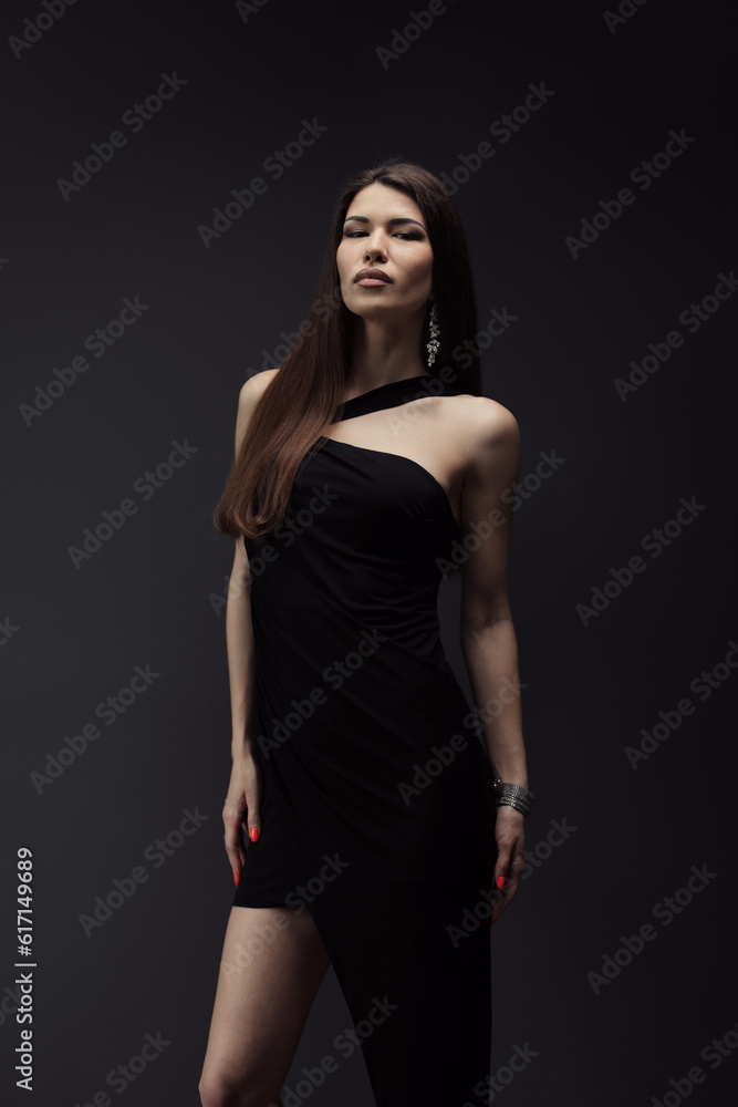 Sensual young female in stylish black dress standing in studio and looking at camera on black background during photo shoot against dark backdrop Sensual young female in stylish black dress standing in studio and looking at camera on black background during photo shoot against dark backdrop