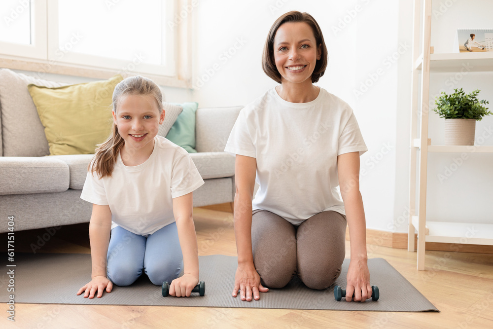 Positive millennial caucasian woman in sportswear and teenage daughter training with dumbbells together