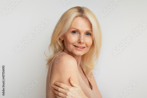 Portrait of attractive mature lady embracing herself and smiling at camera, beautiful aged woman with smooth skin