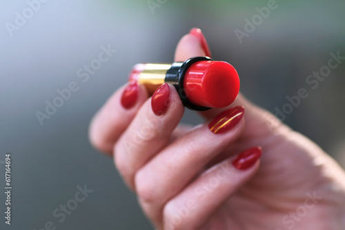 Red lipstick in female hand with red manicure, hand with lipstick photo