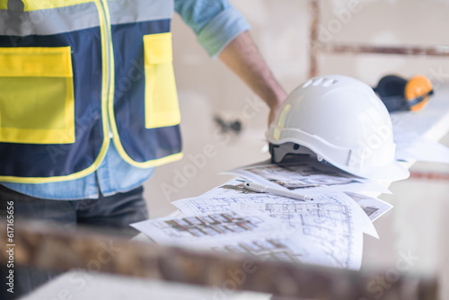 Worker in professional uniform putting hardhat on heap of project documents construction equipment and safety rules during renovation process in premise