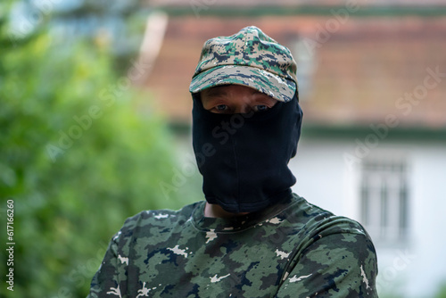 Military mercenary, balaclava hides his face, camouflage uniform, on a blurry background of city buildings. Concept: private military company, armed conflict, war in Ukraine. photo