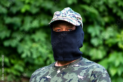 Military mercenary in balaclava and camouflage on a blurry background of green forest. 