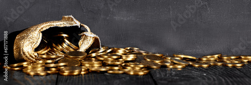 A bag with gold coins on a wooden background banner. The money is in a black bag. Treasure Hunt. A Purse with money on a black background. Wallet wit gold coins.