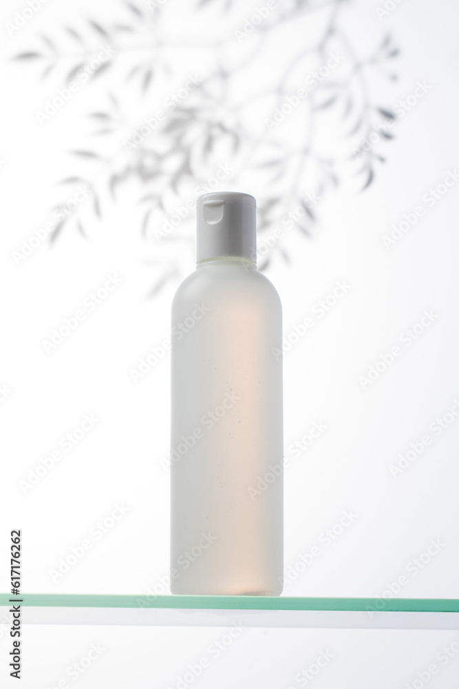 A bottle with a natural cosmetic product on a glass shelf and a shadow on the plants. A bottle with a natural cosmetic product on a glass shelf and a shadow on the plants.