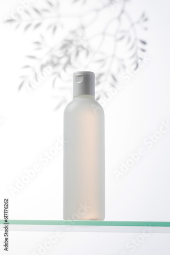 A bottle with a natural cosmetic product on a glass shelf and a shadow on the plants.