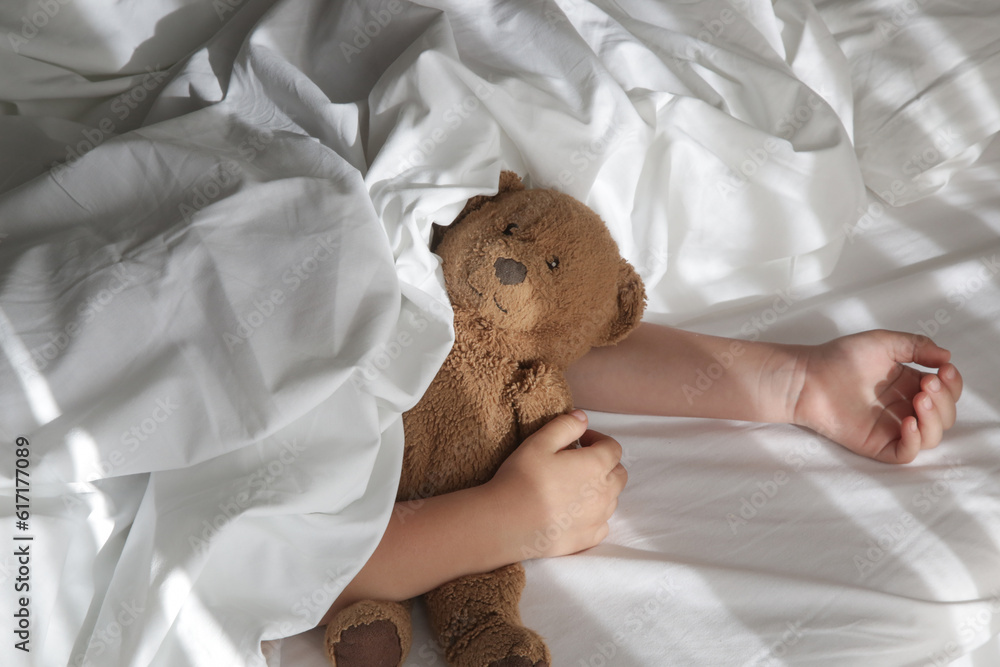 Child sleeping under white sheets hugging teddy bear. Children's nap time or bedtime.