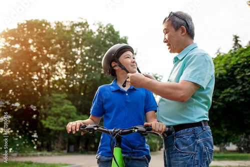 Fotografija father puts protective helmet on his Asian son's head, Korean boy rides bike wit
