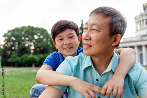 portrait of asian old father with little son outdoors, korean boy hugging grandpa and smiling in park