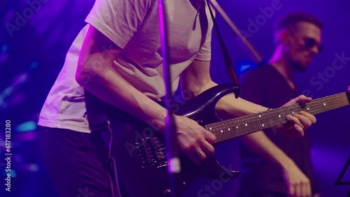 A virtuoso guitarist playing an electric guitar on stage with flashing neon lights. Man is playing guitar on stage. Young man playing on electric guitar