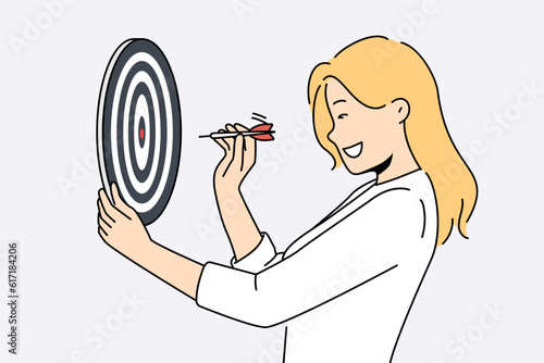 Determined woman throws darts at target for concept of business success and achieving set goals. Goal oriented businesswoman with darts board smiling setting and achieving ambitious goals
