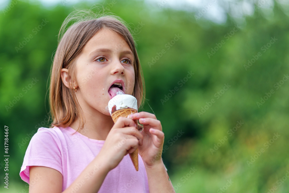 Cute little girl eating an ice cream cone holding it with both hands in summer in the park. High quality photo, blurred background Cute little girl eating an ice cream cone holding it with both hands in summer in the park. High quality photo, blurred background