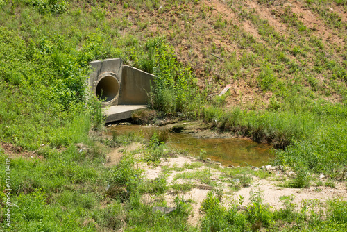 Drainage ditch lined with grass and weeds behind a subdivision