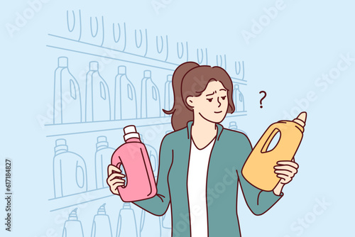 Woman holds bottles of laundry detergent or cleaning product standing near shelves in grocery supermarket. Girl visitor to supermarket compares goods choosing best option for purchase