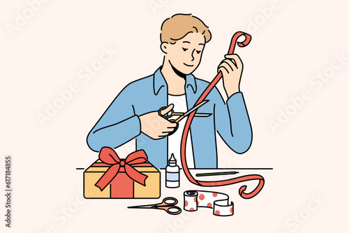 Man makes gift with own hands decorating box with red ribbon with festive paper. Romantic guy prepares beautiful DIY gift for valentine day and birthday and christmas for beloved girlfriend