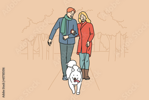 Man and woman are walking their dog together in park enjoying walk on autumn evening with warm weather. Happy couple with white dog on leash take care of pet in need of timely walk outdoors