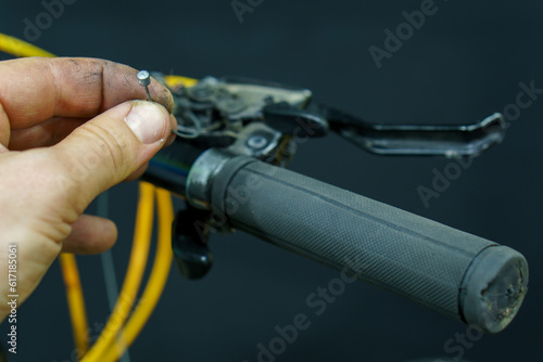 The handlebar of a mountain bike in the workshop on a black background. Replacement of the gearshift cable in the bike. The mechanic has a new cable in his hands.