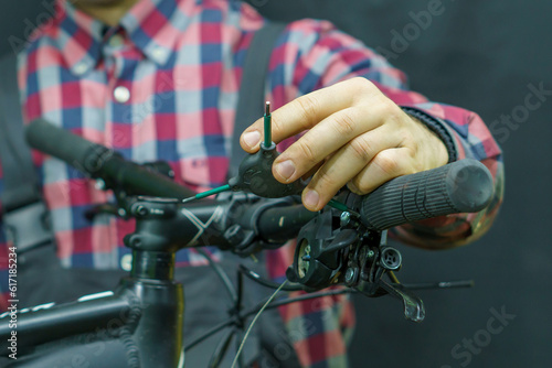 Portrait of a young mechanic in a plaid shirt on a black background in the process of work. A bicycle mechanic holds a tool and a spare part for a mountain bike in his hands. Replacing the shifter © Pokoman