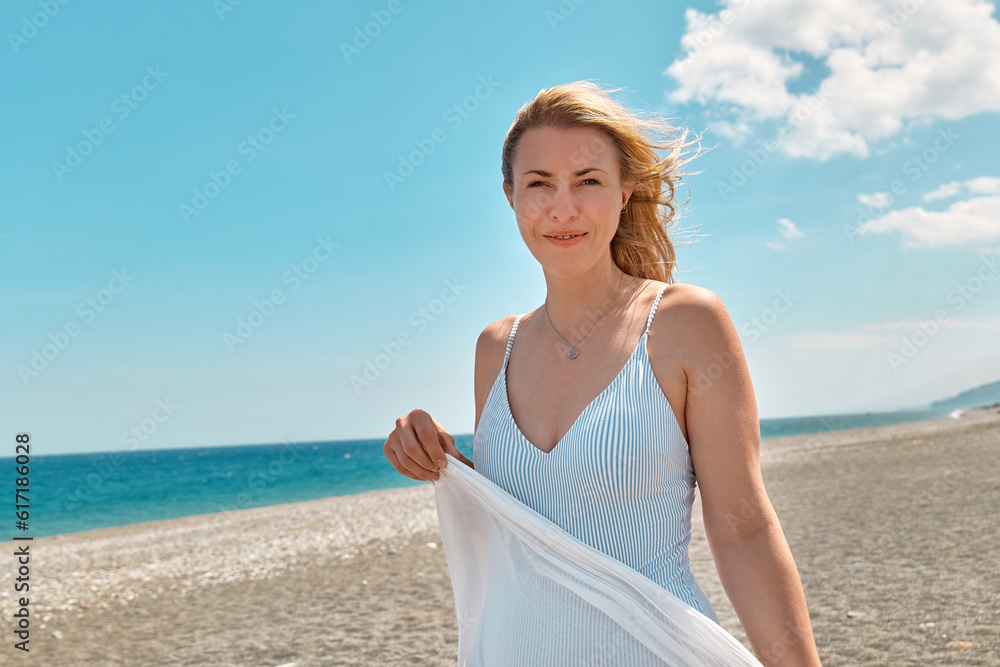 Pretty blond woman in swimsuit and white pareo enjoying sunny windy day near blue sea. Happy female enjoying the life. Beach summer, travel concept. Pretty blond woman in swimsuit and white pareo enjoying sunny windy day near blue sea. Happy female enjoying the life. Beach summer, travel concept.