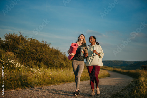 Fototapeta Naklejka Na Ścianę i Meble -  Sisterhood of Serenity: Two women, representing different ethnicities, radiate tranquility and unity as they prepare to engage in a yoga session surrounded by nature's splendor.