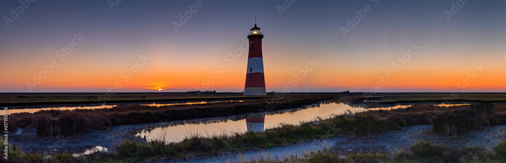 big lighthouse in the middle of a meadow and a river with a beautiful sunset