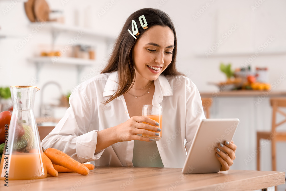 Young woman with glass of vegetable juice using tablet computer in kitchen Young woman with glass of vegetable juice using tablet computer in kitchen