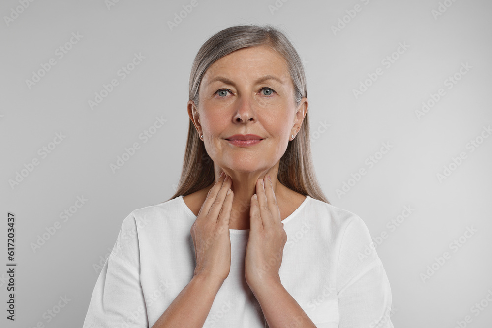 Endocrine system. Senior woman doing thyroid self examination on light grey background Endocrine system. Senior woman doing thyroid self examination on light grey background